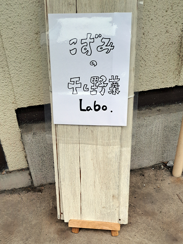 横浜市金沢区の一角。地元アパートの所有者の協力で２０２４年６月にオープンさせた「こずみの干し野菜Labo」の入り口。手作りの看板に温かみを感じます。